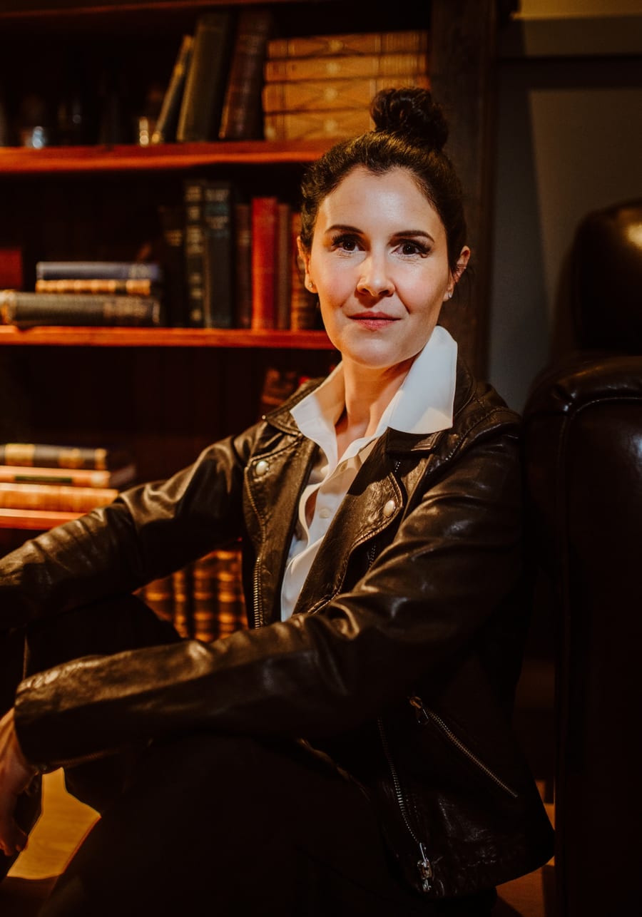 Mary Jane Howie sitting in a leather chair in front of a shelf of old books.